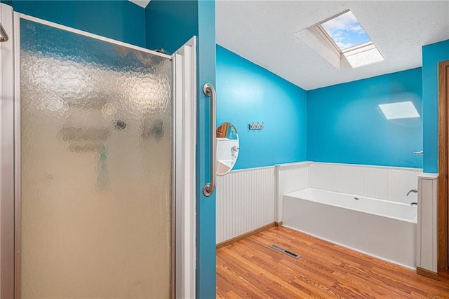 full bathroom featuring visible vents, wood finished floors, a skylight, a shower stall, and wainscoting