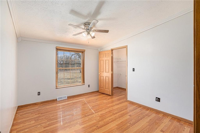 unfurnished bedroom with light wood-type flooring, a textured ceiling, visible vents, and ornamental molding