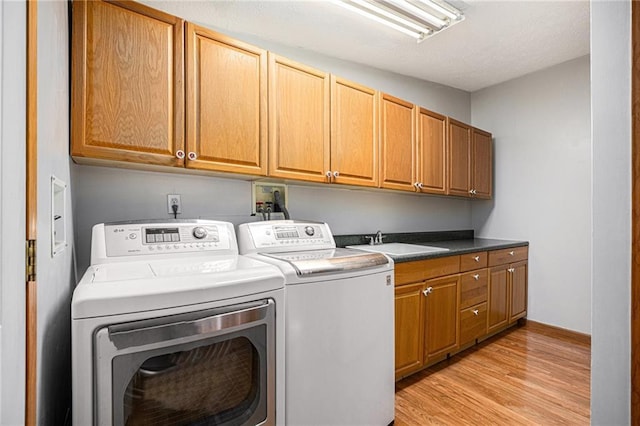 washroom with light wood-type flooring, a sink, a textured ceiling, cabinet space, and washing machine and clothes dryer