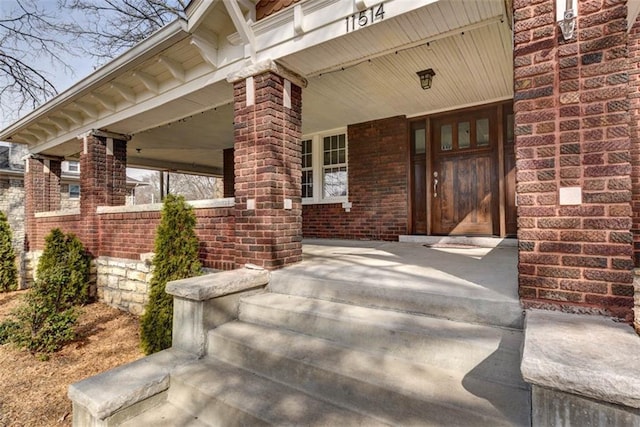 doorway to property featuring covered porch and brick siding