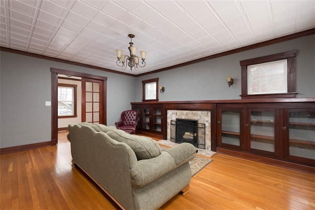 living area featuring a chandelier, crown molding, light wood-style flooring, and baseboards