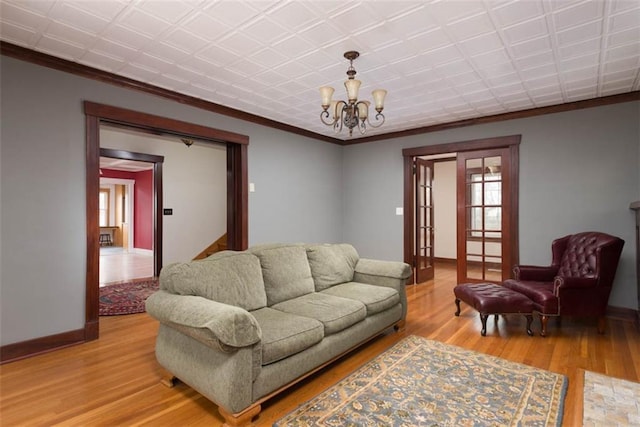 living area with light wood-type flooring, crown molding, baseboards, and an inviting chandelier