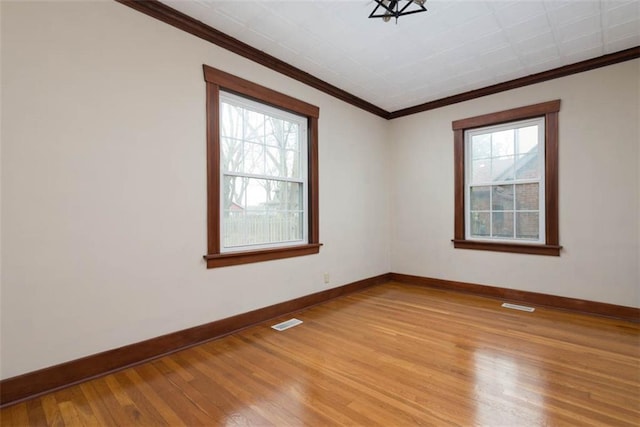 empty room featuring ornamental molding, light wood-style flooring, a wealth of natural light, and baseboards