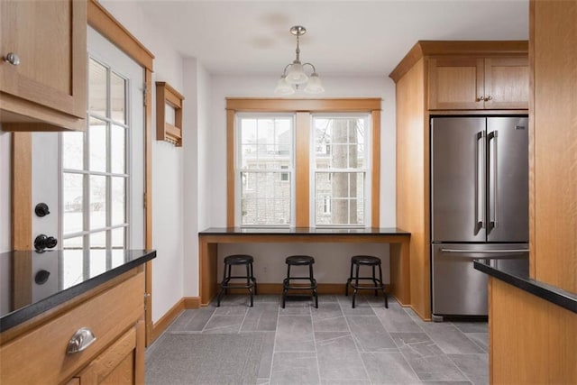 kitchen with dark countertops, a healthy amount of sunlight, high end fridge, and hanging light fixtures