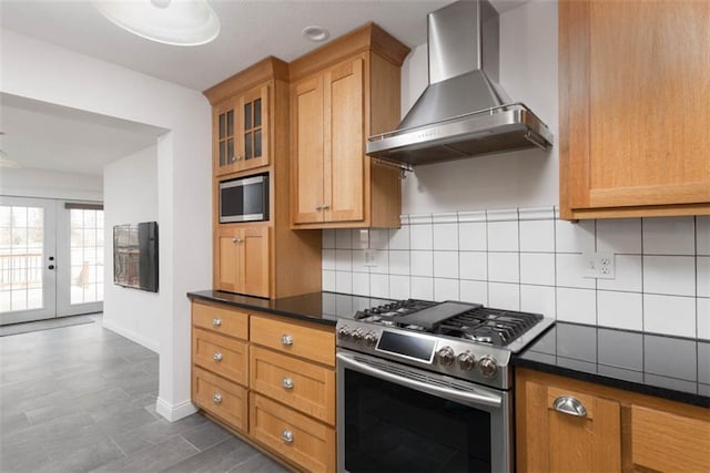 kitchen with brown cabinets, backsplash, glass insert cabinets, gas range, and wall chimney exhaust hood