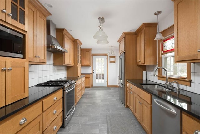 kitchen with wall chimney range hood, appliances with stainless steel finishes, decorative backsplash, and a sink