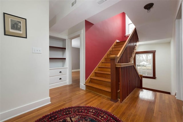 staircase featuring wood finished floors, visible vents, and baseboards