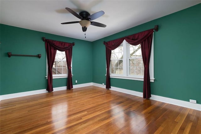 empty room with wood finished floors, a ceiling fan, and baseboards