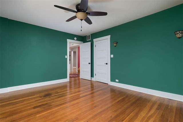 spare room featuring baseboards, visible vents, ceiling fan, and wood finished floors