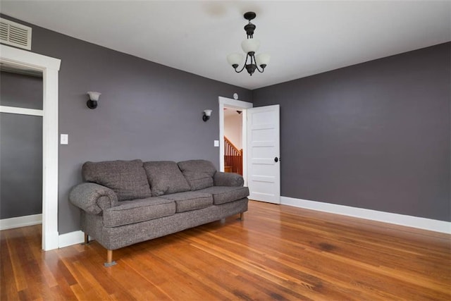 living area featuring a chandelier, visible vents, baseboards, and wood finished floors