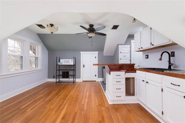 kitchen featuring light wood finished floors, visible vents, white microwave, white cabinetry, and a sink