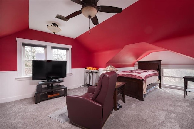 carpeted bedroom with lofted ceiling, a wainscoted wall, ceiling fan, and visible vents