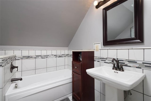 bathroom with lofted ceiling, a sink, a bath, and tile walls