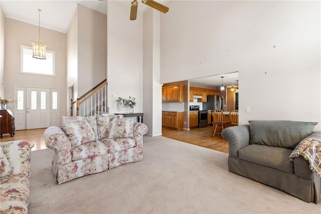 living area with light carpet, a high ceiling, stairs, and ceiling fan with notable chandelier