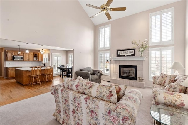 living area with a ceiling fan, high vaulted ceiling, a tile fireplace, light wood-style floors, and light carpet