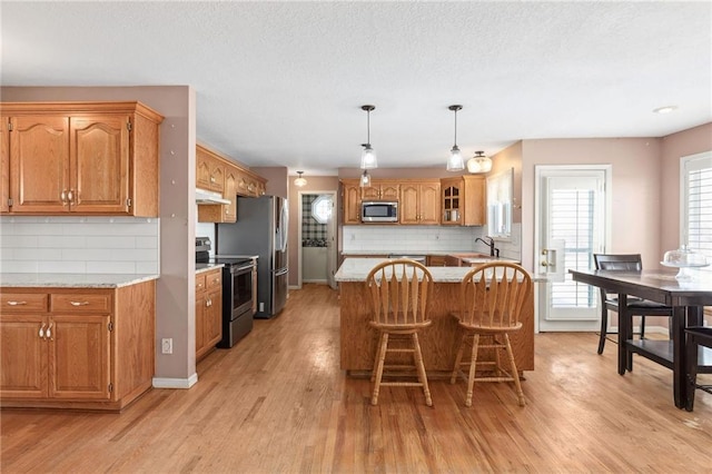 kitchen featuring under cabinet range hood, stainless steel appliances, light wood-style floors, and a sink