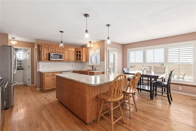 kitchen with light wood finished floors, backsplash, a kitchen island, glass insert cabinets, and appliances with stainless steel finishes