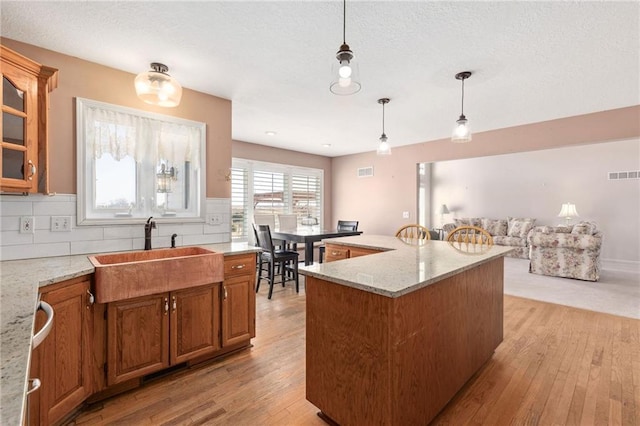 kitchen featuring brown cabinets, visible vents, light wood finished floors, and a sink