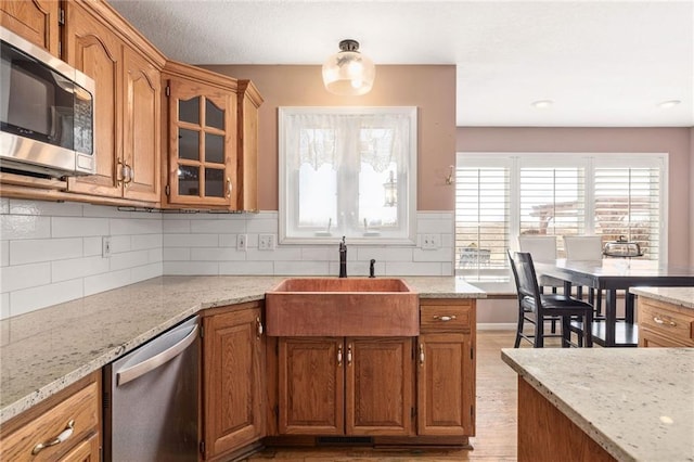 kitchen with a sink, glass insert cabinets, appliances with stainless steel finishes, and brown cabinetry