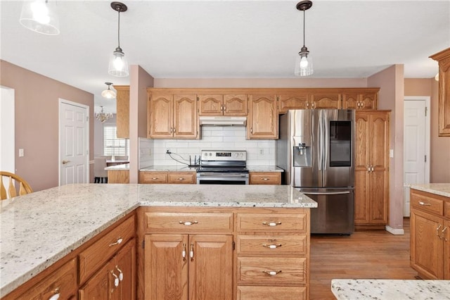 kitchen with light stone countertops, under cabinet range hood, decorative backsplash, appliances with stainless steel finishes, and light wood-style floors