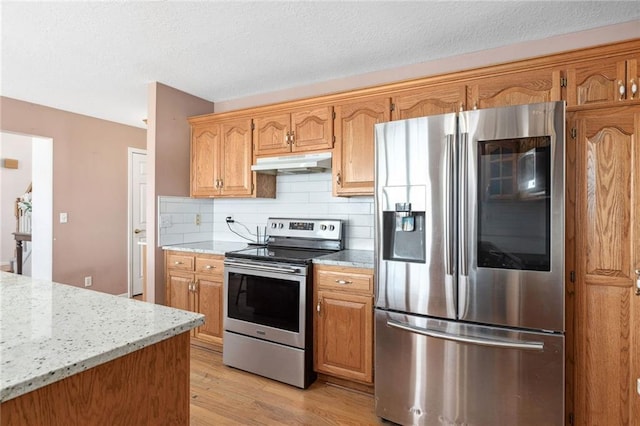 kitchen with tasteful backsplash, under cabinet range hood, light wood-style flooring, appliances with stainless steel finishes, and a textured ceiling