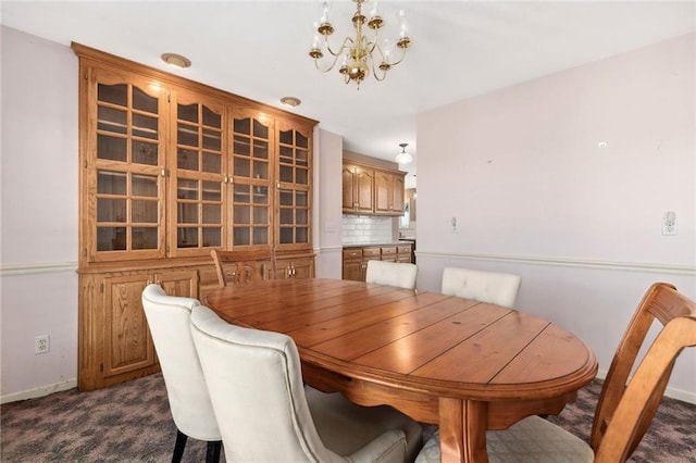 dining area with a chandelier, dark carpet, and baseboards