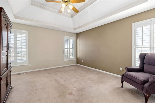 living area featuring a raised ceiling, a healthy amount of sunlight, light colored carpet, and baseboards