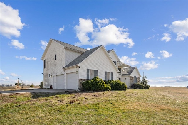 view of side of home featuring a garage, stone siding, a lawn, and driveway