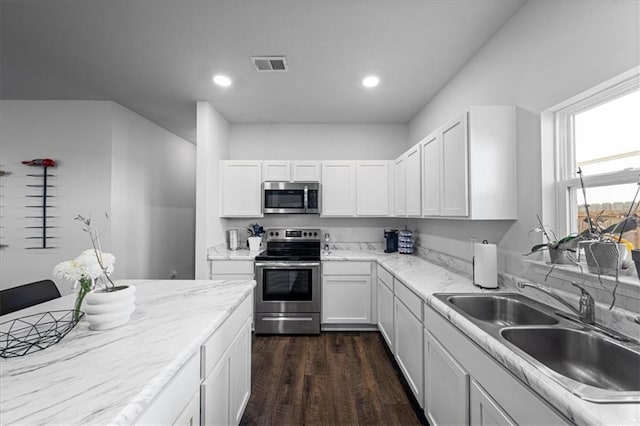 kitchen with dark wood-style flooring, visible vents, appliances with stainless steel finishes, white cabinets, and a sink