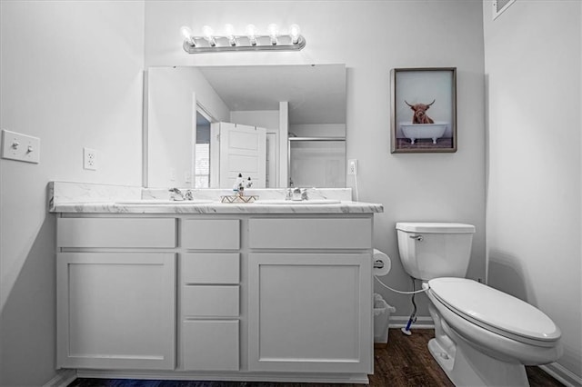 full bath featuring double vanity, toilet, a stall shower, a sink, and wood finished floors