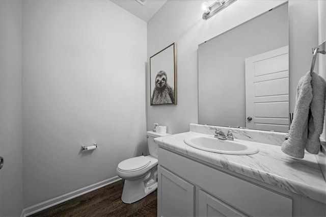 half bathroom with vanity, wood finished floors, toilet, and baseboards