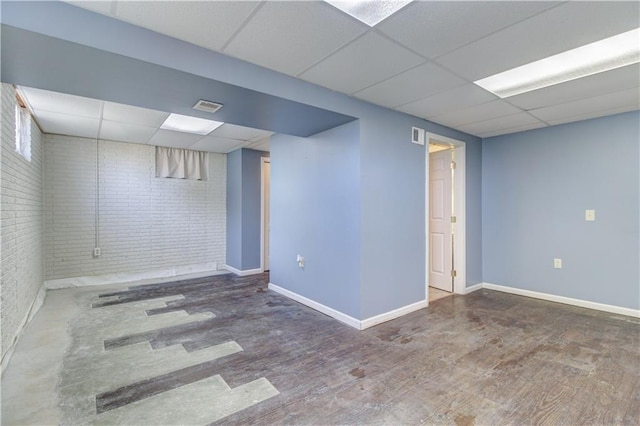 finished basement with a paneled ceiling, brick wall, wood finished floors, visible vents, and baseboards