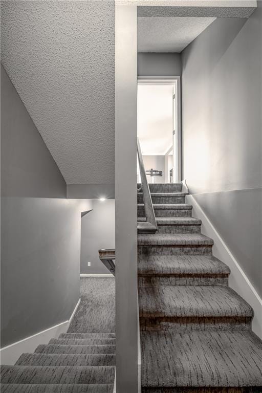 stairway featuring carpet flooring, a textured ceiling, and baseboards