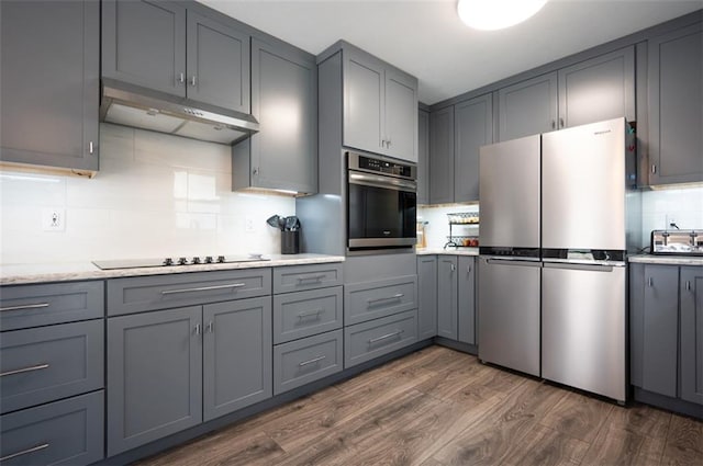 kitchen featuring under cabinet range hood, gray cabinetry, stainless steel appliances, dark wood-style flooring, and backsplash