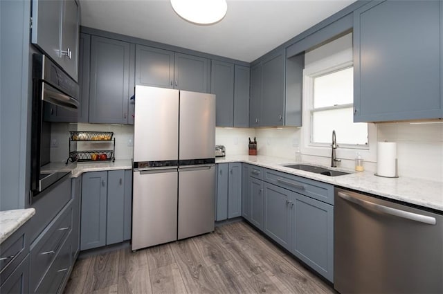 kitchen featuring dark wood-style floors, decorative backsplash, appliances with stainless steel finishes, a sink, and light stone countertops