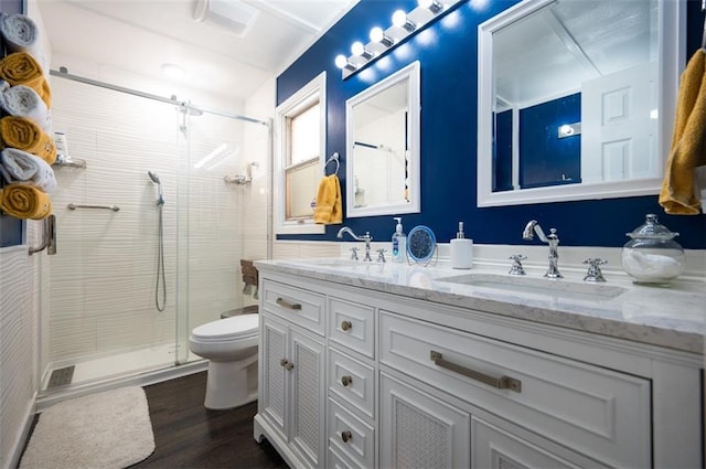 bathroom with double vanity, toilet, a stall shower, a sink, and wood finished floors