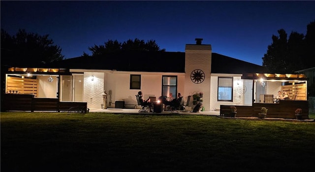 back of house at twilight with stucco siding, a lawn, and a patio