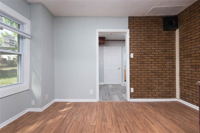 unfurnished room with baseboards, brick wall, and wood finished floors