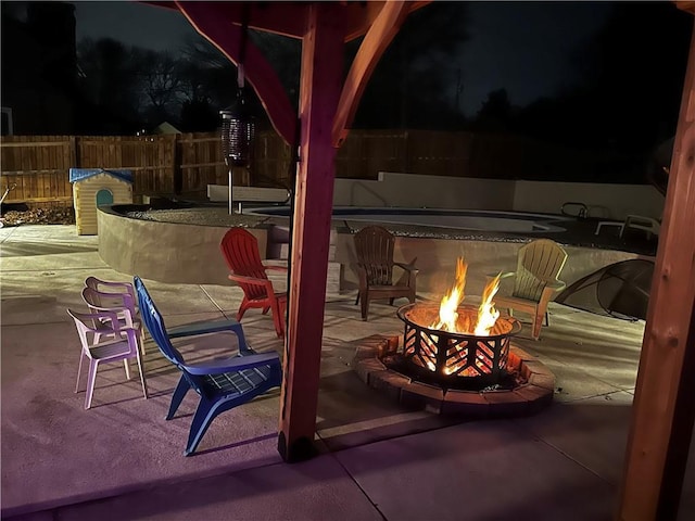 patio at night featuring an outdoor fire pit and fence