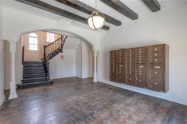 foyer entrance featuring arched walkways, hardwood / wood-style flooring, stairway, beamed ceiling, and mail area