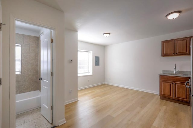 unfurnished dining area featuring light wood-style flooring, electric panel, baseboards, and a sink