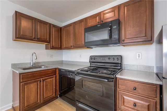 kitchen with light countertops, brown cabinetry, a sink, light wood-type flooring, and black appliances