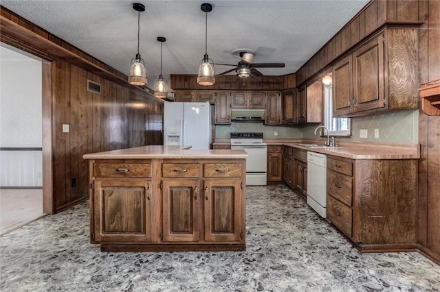 kitchen featuring white appliances, a sink, light countertops, wood walls, and under cabinet range hood