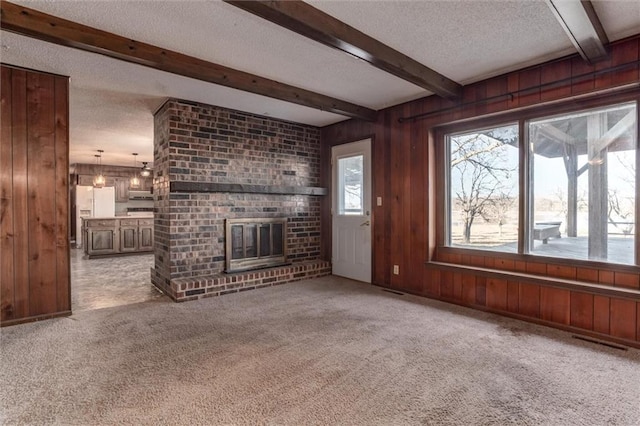 unfurnished living room featuring carpet floors, a textured ceiling, beam ceiling, and wooden walls