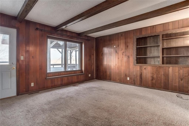 unfurnished living room with beamed ceiling, wooden walls, carpet, and a textured ceiling