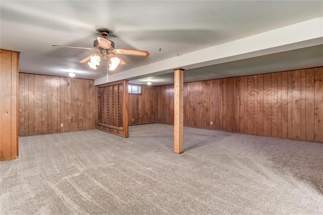 below grade area featuring carpet, wood walls, and a ceiling fan