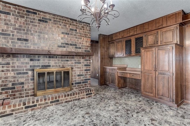 unfurnished living room with a brick fireplace, light colored carpet, an inviting chandelier, a textured ceiling, and built in study area