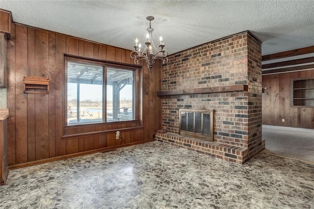 unfurnished living room featuring a chandelier, a textured ceiling, wood walls, and a fireplace