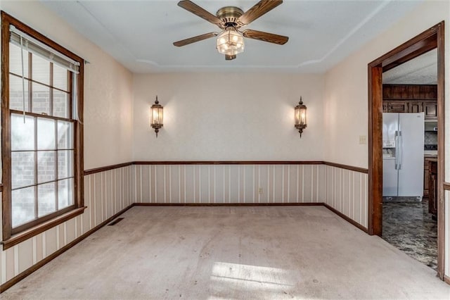 carpeted spare room featuring plenty of natural light, visible vents, and a ceiling fan