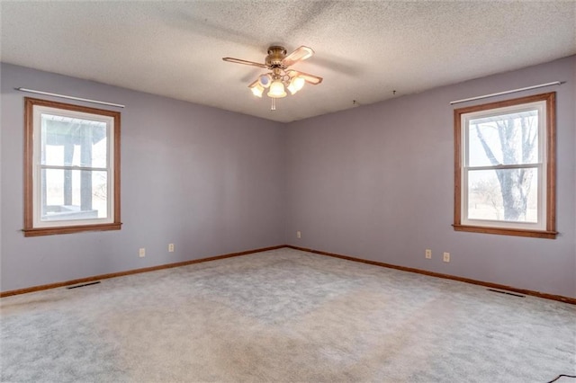 carpeted empty room featuring visible vents, a textured ceiling, a healthy amount of sunlight, and a ceiling fan